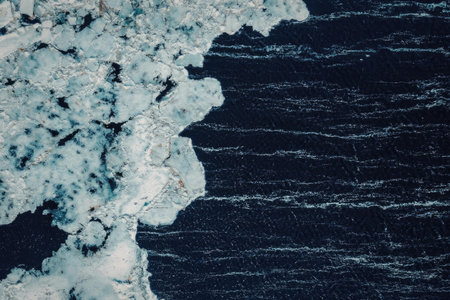 An aerial view of ice and ocean water meeting, showcasing the contrast between the white, foamy ice...