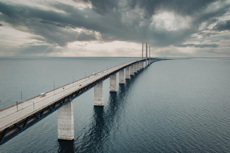 A long bridge stretches over calm water under a cloudy sky, showcasing a serene and peaceful scene.
