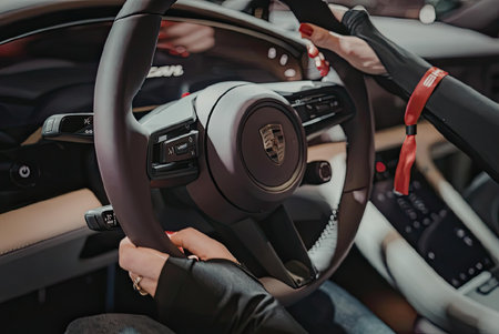 A person is holding the steering wheel of a car with both hands, wearing a watch on their left...