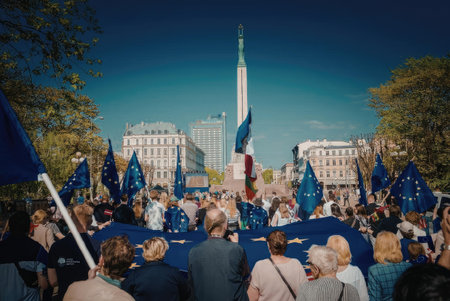 A crowd of people gathered for a rally or protest, holding blue flags and signs. The scene is set...