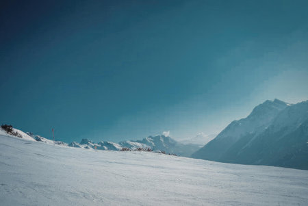 A serene snowy mountain landscape under a clear blue sky, with snow-covered mountains in the...