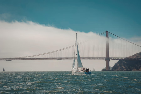 A white sailboat on the water with the Golden Gate Bridge in the background, covered in fog.