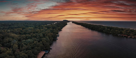 A tranquil river scene at sunset, with a vibrant sky reflecting on the water's surface, surrounded...