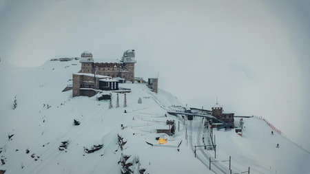 A snowy mountain resort with a ski lift on a foggy day, featuring buildings and slopes covered in...
