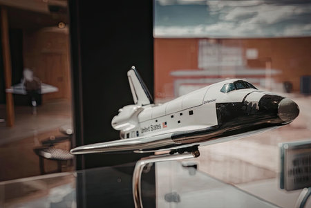 A model of a space shuttle on display in a glass case, with a blurred background of a museum or...