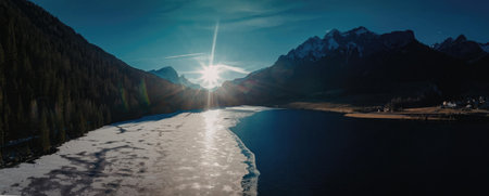 a frozen lake with snow covered mountains and a sun rising over the horizon