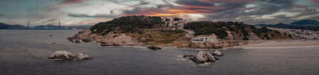 A panoramic view of a small island with a vibrant sunset in the background, featuring a rocky...