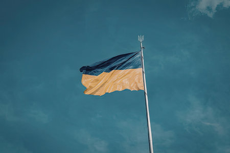 The Ukrainian flag is prominently displayed against a clear blue sky with a few wispy clouds. The...