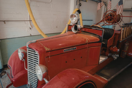 A vintage red fire truck is parked in a garage with its front end facing the camera. The truck has a...