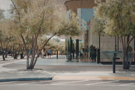 A blurry image of people walking on a sidewalk outside a building with trees and a road in the foreground.の写真素材