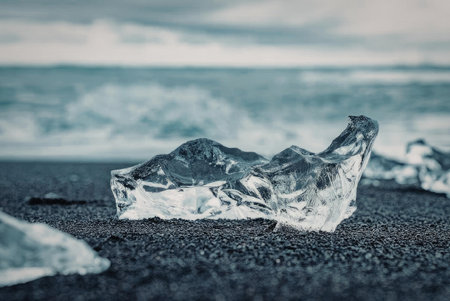 A piece of clear ice on a black sand beach with ocean waves in the background.の写真素材