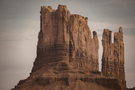 A majestic rock formation in Monument Valley with towering brown rock structures against a cloudy...