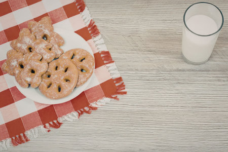 A plate of chocolate chip cookies on a red and white checkered cloth next to a glass of milk on a...