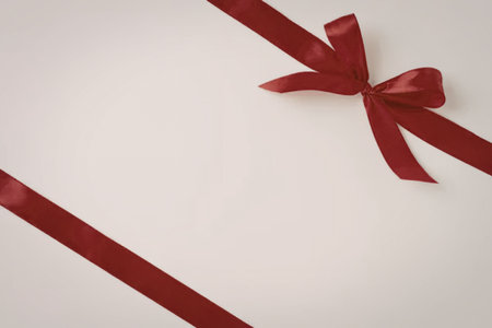 A close-up image of a red ribbon tied in a bow on a white background, with one end of the ribbon extending diagonally across the image.の写真素材