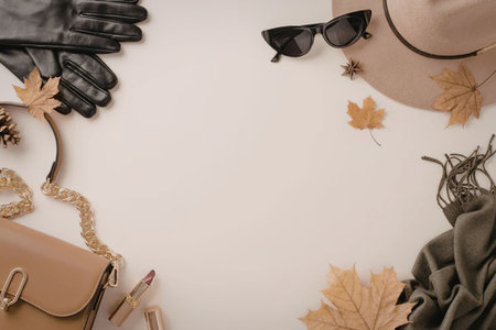 A flat lay of fashion accessories for autumn, including a hat, sunglasses, gloves, a purse, and clothing items, surrounded by fall leaves.の写真素材