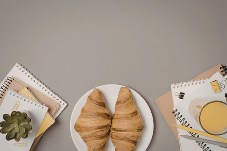 A plate with two croissants, a glass of orange juice, and notebooks on a gray table.の写真素材