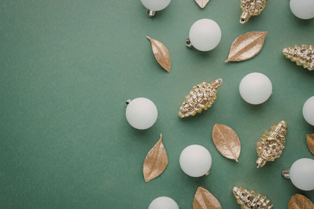 A festive arrangement of white Christmas ornaments, gold leaves, and pinecones on a green...