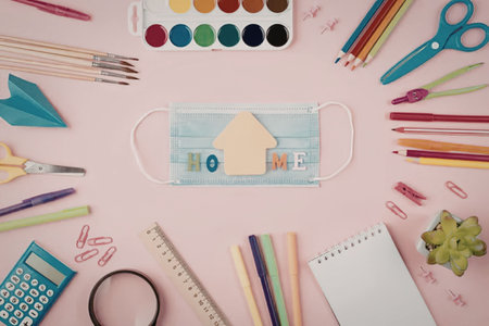 A flat lay of colorful school supplies, including a face mask with a house design, on a pink...