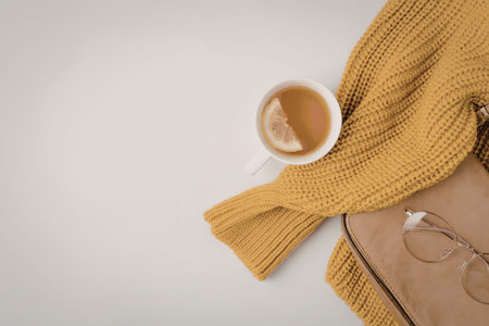 A serene still life arrangement featuring a cup of tea, a vibrant yellow sweater, a tan bag, and...