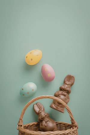 A wicker Easter basket with chocolate bunny and eggs on a green background