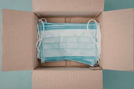 A cardboard box opened to reveal a collection of blue and white face masks inside.