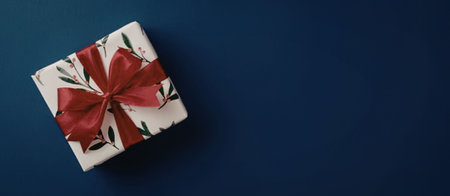 A gift box wrapped in white paper with a red bow on a blue backgroundの写真素材