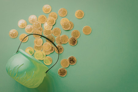 A green bucket lies on its side with gold coins spilling out onto a green background.の写真素材