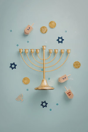 A gold menorah surrounded by dreidels and gold coins on a light blue background, representing the Jewish holiday of Hanukkah.の写真素材