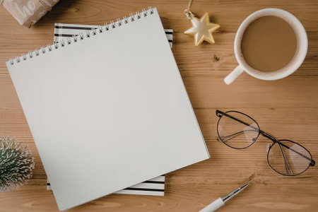 A morning desk setup with a cup of coffee, a blank notebook, glasses, and a pen on a wooden desk.