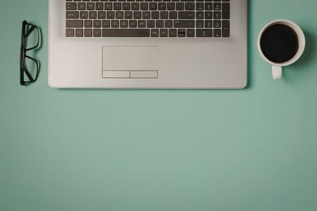 A minimalist workspace setup featuring a laptop, coffee, and glasses on a green desk.