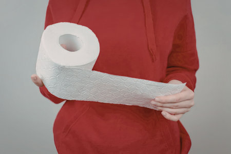 A person wearing a red hoodie holding a large roll of toilet paper