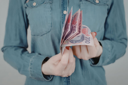 A person wearing a blue denim shirt holding banknotes in their hands.