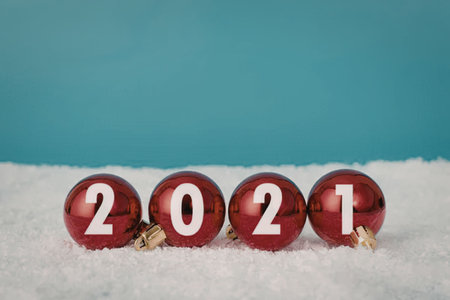 Three red Christmas ornaments with gold caps and white numbers 2, 0, 2, 1 spelling out 2021, sitting...