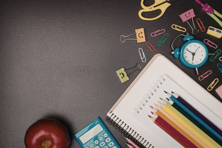 A collection of school supplies including a notebook, colored pencils, calculator, apple, and...
