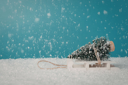 A small Christmas tree on a white sled in snowy conditions with a blue background