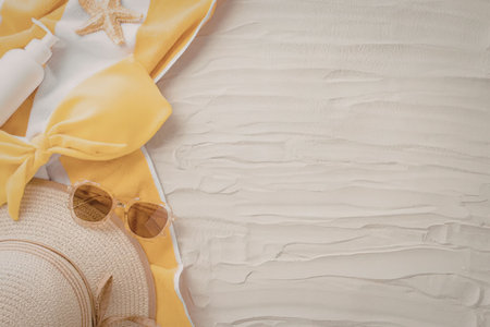 A serene beach scene featuring a straw hat, sunglasses, and a yellow and white bikini top on sand.