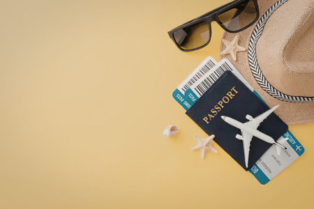 A flat lay of travel essentials including a passport, sunglasses, a hat, and starfish on a yellow...