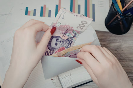 A person with red-painted nails handling banknotes on a desk with a colorful bar graph in the...
