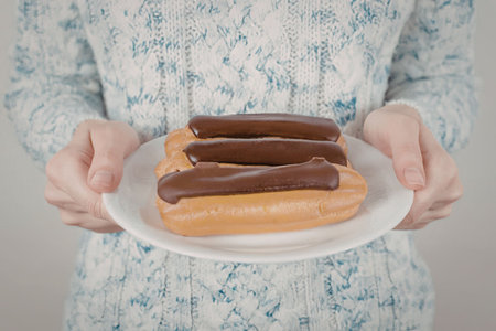 A woman in a blue and white dress holding a plate of chocolate eclairs.
