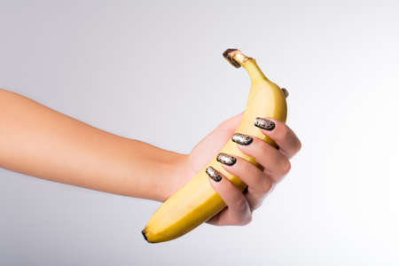 hand with painted nails clutching a bananaの写真素材