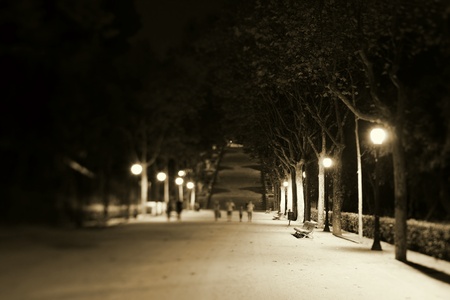 Nightscene with an illuminated park bench and walkway with distant pedestriansのeditorial素材