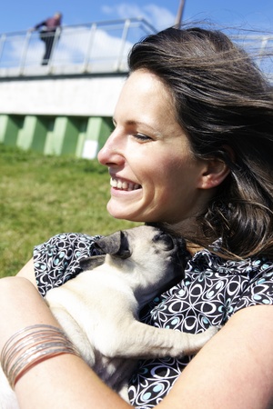 Close up of a smiling woman hugging a young pug puppy to her chest