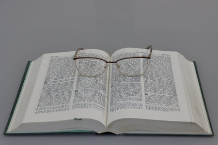 Book with glasses on a gray background, close-up, vertical