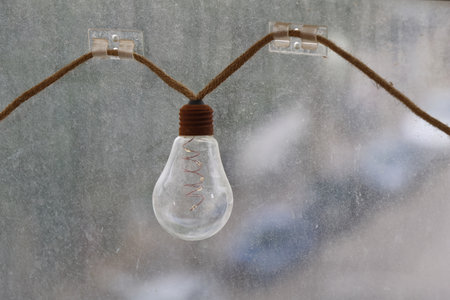 Light bulb hanging on the rope in front of a frozen window.の写真素材