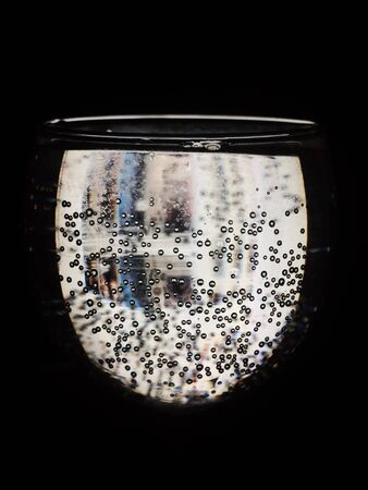 A glass with bubbles through which light passes on a black background.の写真素材