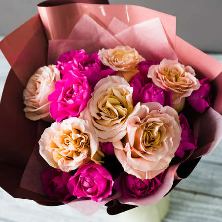 Burgundy bouquet with white and pink roses stands in a white stand on a gray wooden tableの写真素材