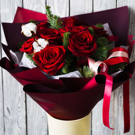 Yellow stand with burgundy bouquet of red roses green branches of a christmas tree with white flowers with pink ribbons on a gray wooden backgroundの写真素材