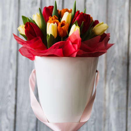 White flowerpot of red yellow orange tulips with red and pink ribbons on gray wooden backgroundの写真素材
