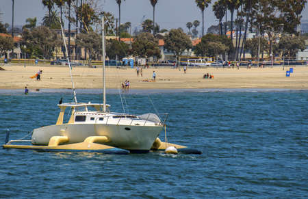 A tri-hull sailboat is anchored off a sunny beach.の写真素材