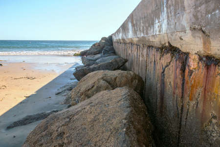A weather-beaten seawall protects a boating channel by a beach in California.の写真素材